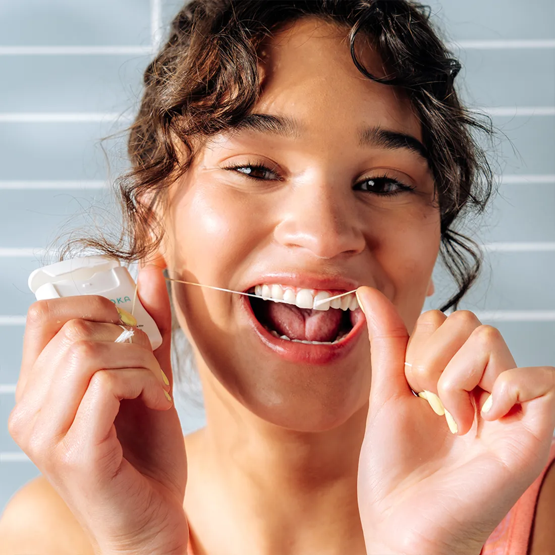 Woman using dental floss with a neutral background