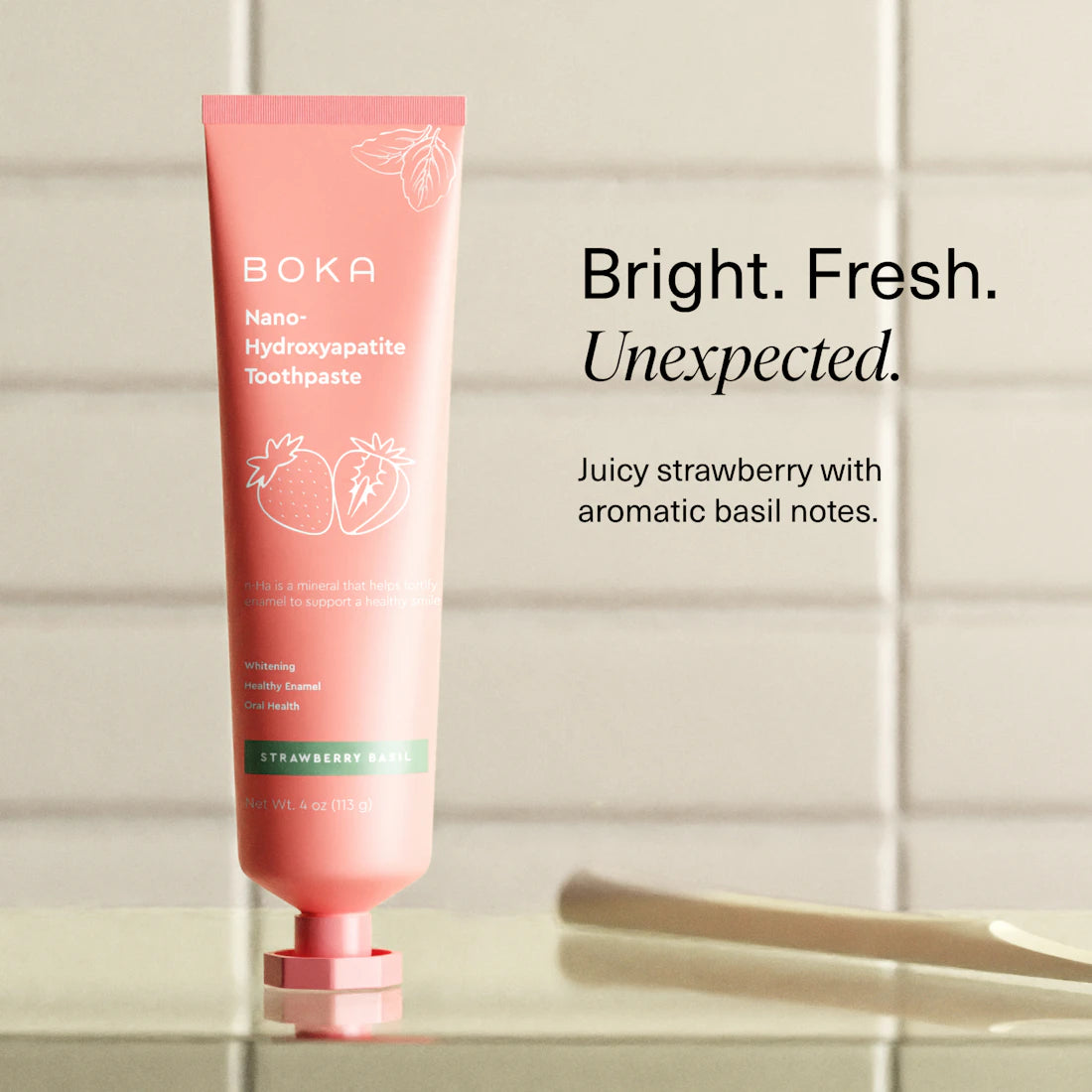 Strawberry Basil n-Ha Toothpaste in a pink tube stands upright on a bathroom counter, text beside it.