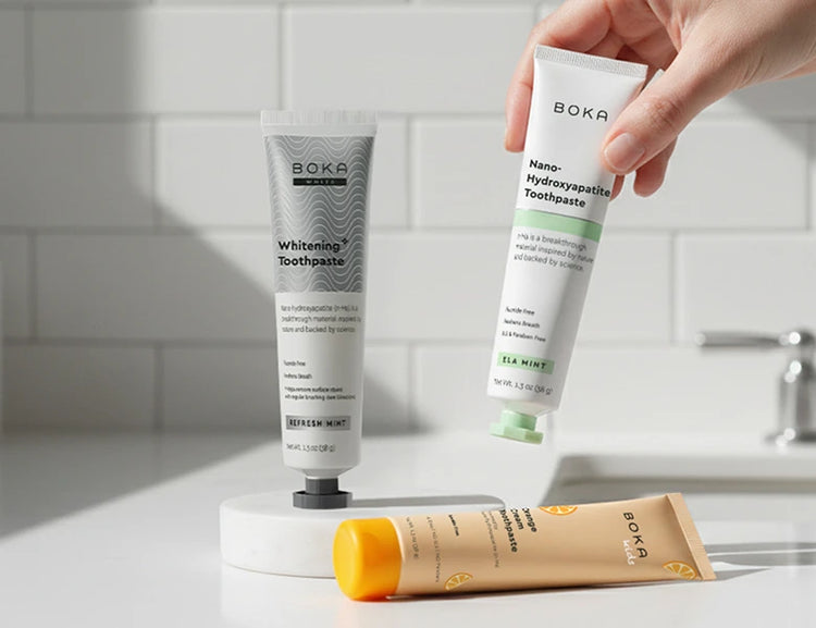 Boka toothpaste tubes on a bathroom counter with a hand holding one tube.