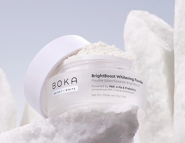 Boka BrightBoost Whitening Powder container on a white towel with a light blue background