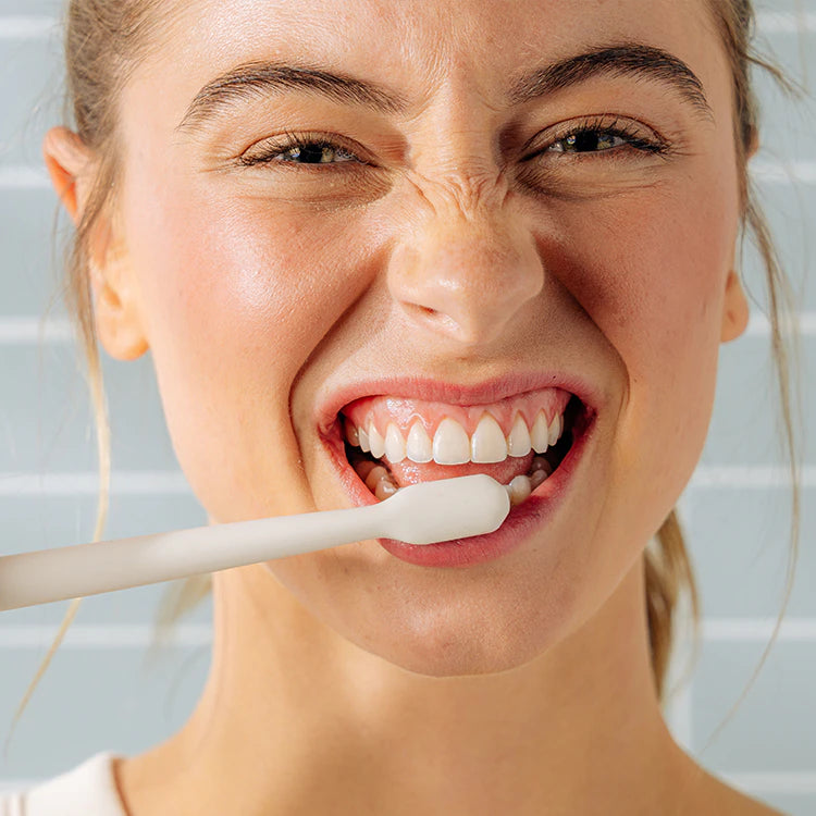 Woman brushing her teeth with a white toothbrush in a bathroom setting