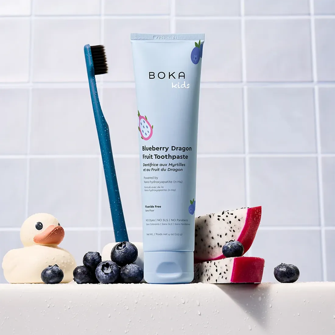 Boka Kids Blueberry Dragon Fruit Toothpaste with a toothbrush and fruit on a tiled background