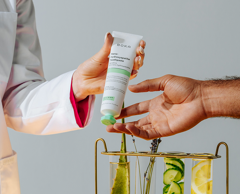 Dentist passing Ela Mint Toothpaste to another person with beakers in background