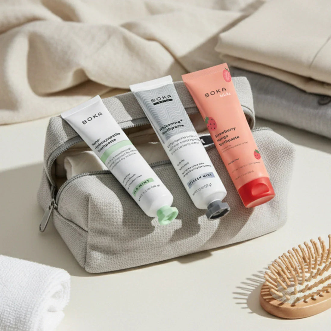 Set of Boka skincare products in a gray pouch with a wooden brush on a light background