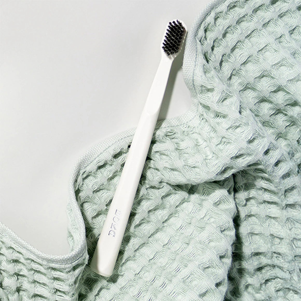 White toothbrush with black bristles on a textured green fabric background