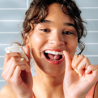 Woman using dental floss with a neutral background