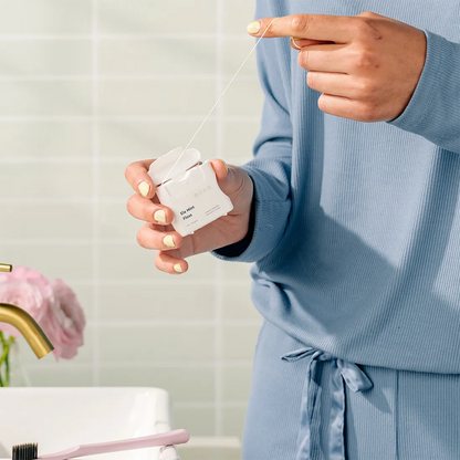 Person holding a Boka Ela Mint Floss, wearing a blue robe in a bathroom setting.