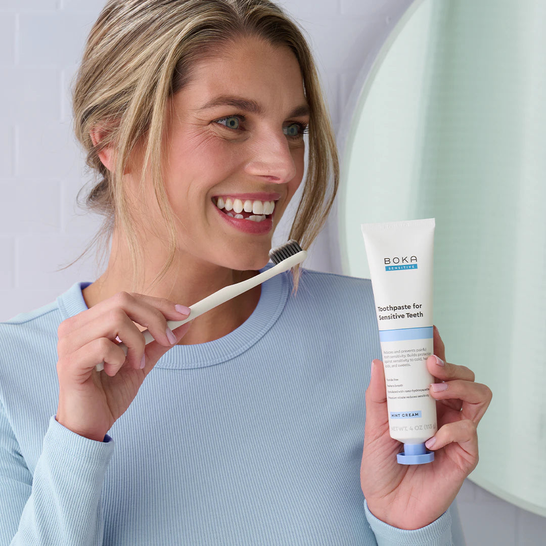 Woman holding a toothbrush and tube of Boka toothpaste with a plain background