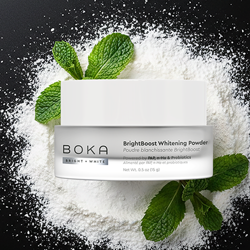 Boka BrightBoost Whitening Powder with mint leaves on a black background