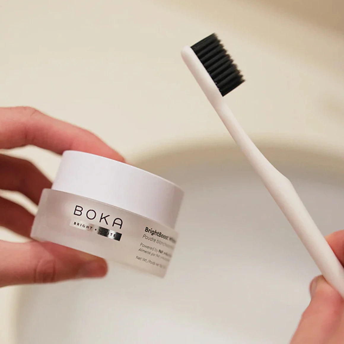 Person holding a Boka skincare product and a toothbrush on a neutral background