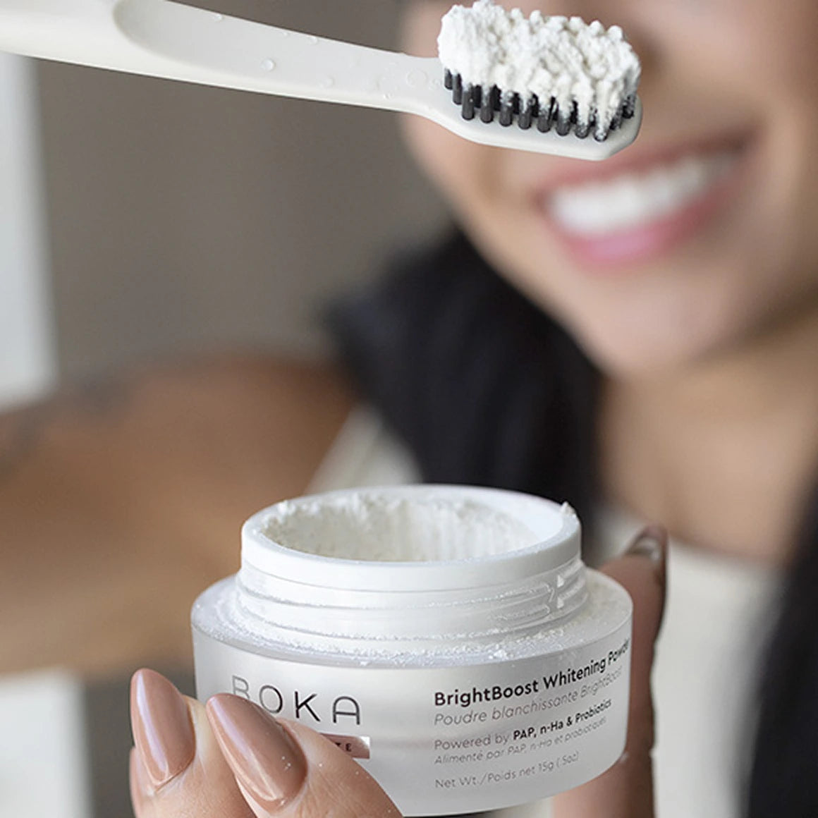 Person holding a jar of Boka BrightBoost Whitening Powder with a toothbrush loaded with powder.
