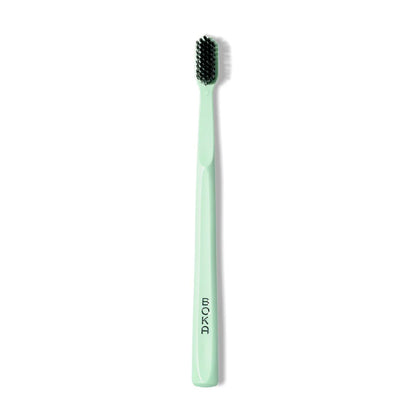 The Classic Toothbrush by BOKA in mint green features black charcoal bristles for a gentle clean.
