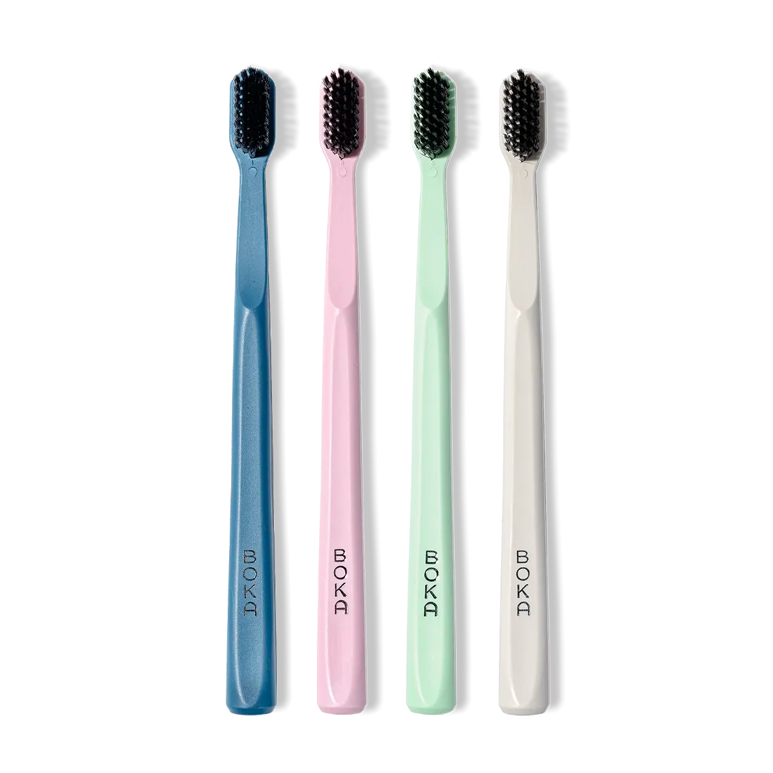 Four toothbrushes in blue, pink, green, and white with black bristles on a white background.