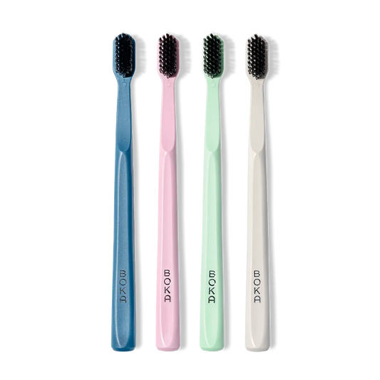 Four toothbrushes in blue, pink, green, and white with black bristles on a white background.