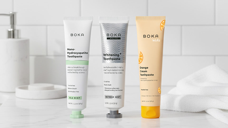 Three Boka toothpaste tubes on a bathroom counter with a tiled wall background.