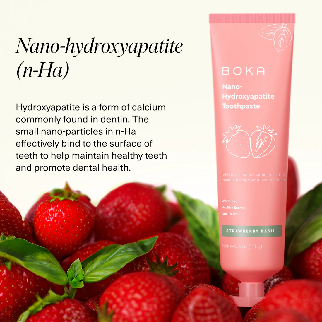 A pink tube of Strawberry Basil n-Ha Toothpaste rests with fresh strawberries and green leaves.