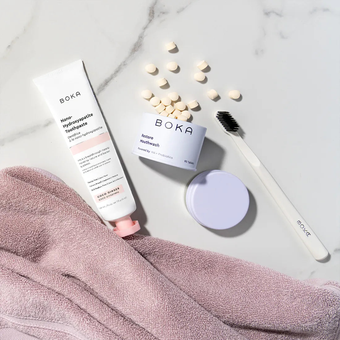 Boka products including a tube, jar, and tablets on a marble surface with a towel.