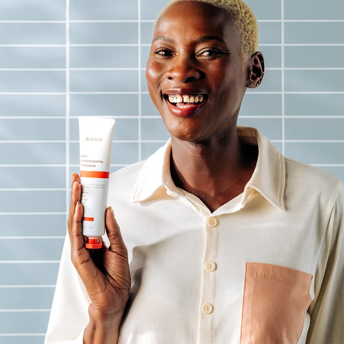 Person holding a Boka toothpaste against a tiled wall background