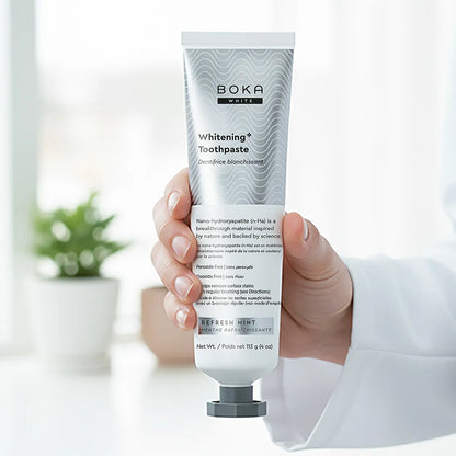 Hand holding a tube of Boka Toothpaste with a blurred indoor background