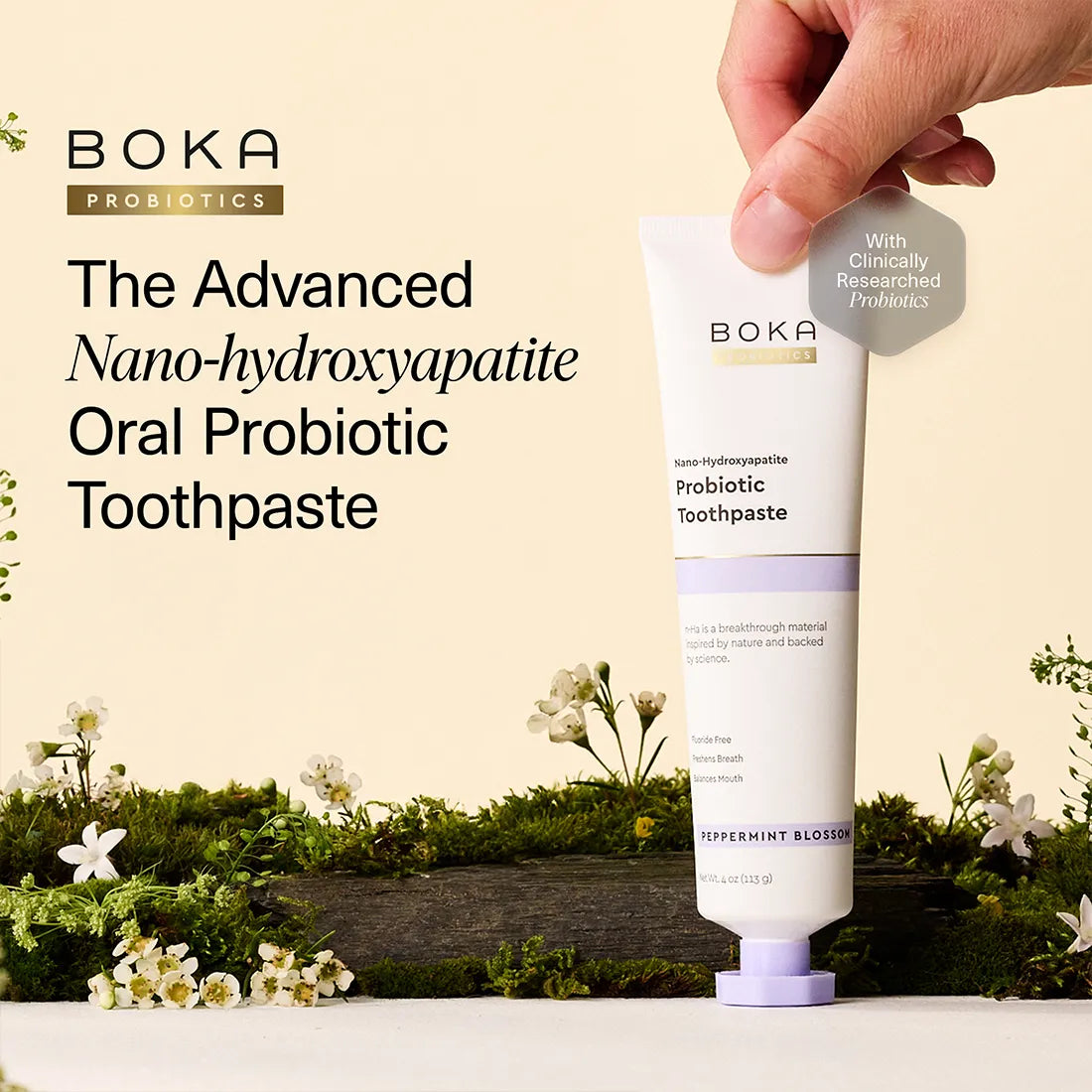 Boka Probiotics toothpaste tube with a hand holding it, set against a natural background with flowers and moss.