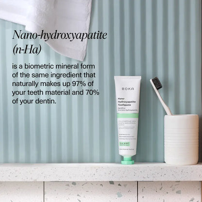 Boka Nano-hydroxyapatite toothpaste tube with a toothbrush on a shelf against a striped wall.