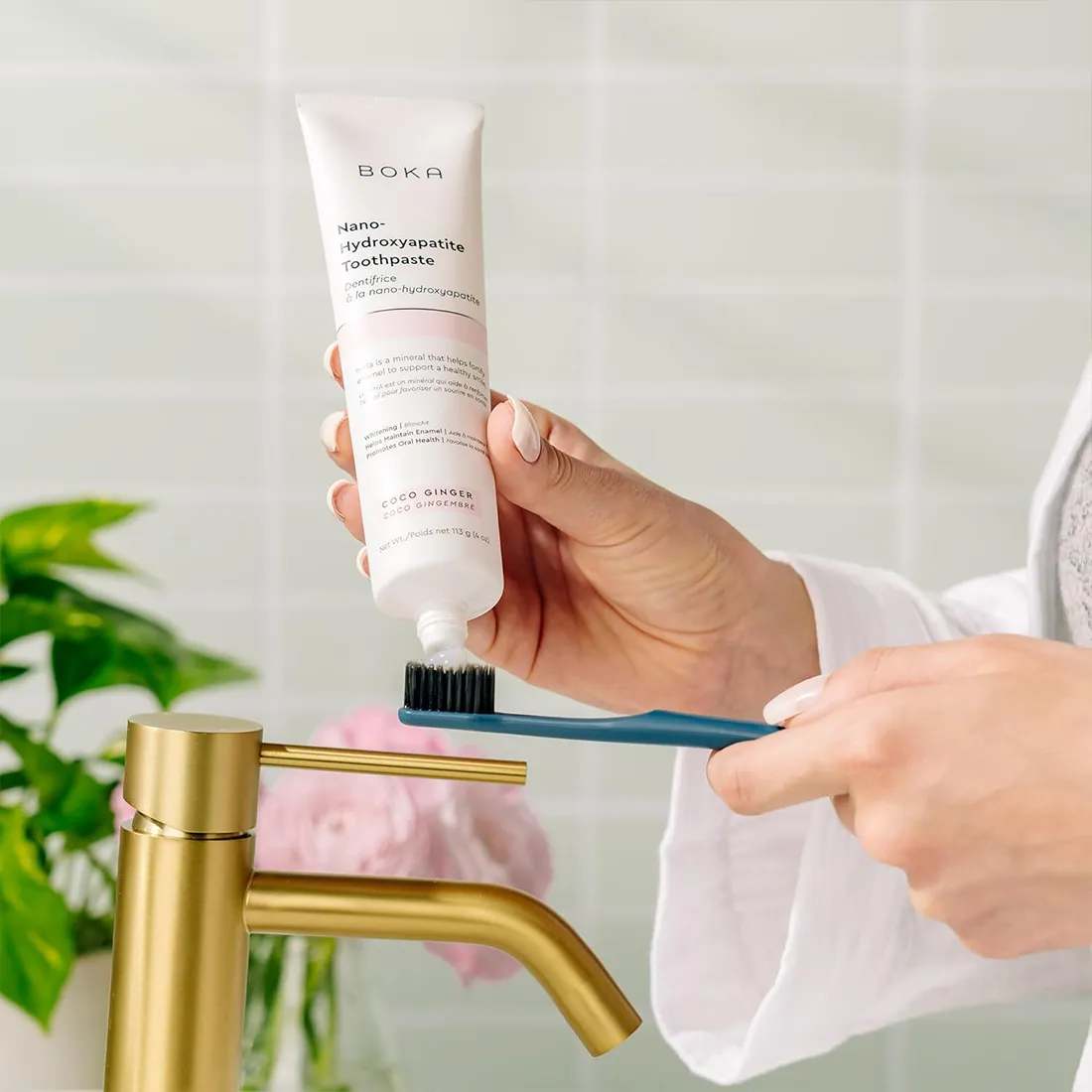 Person applying toothpaste to a toothbrush with a Boka toothpaste tube in a bathroom setting.