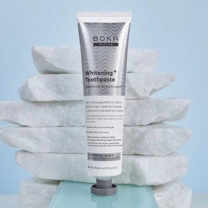 Tube of Boka Whitening Toothpaste on a stack of white stones with a light blue background