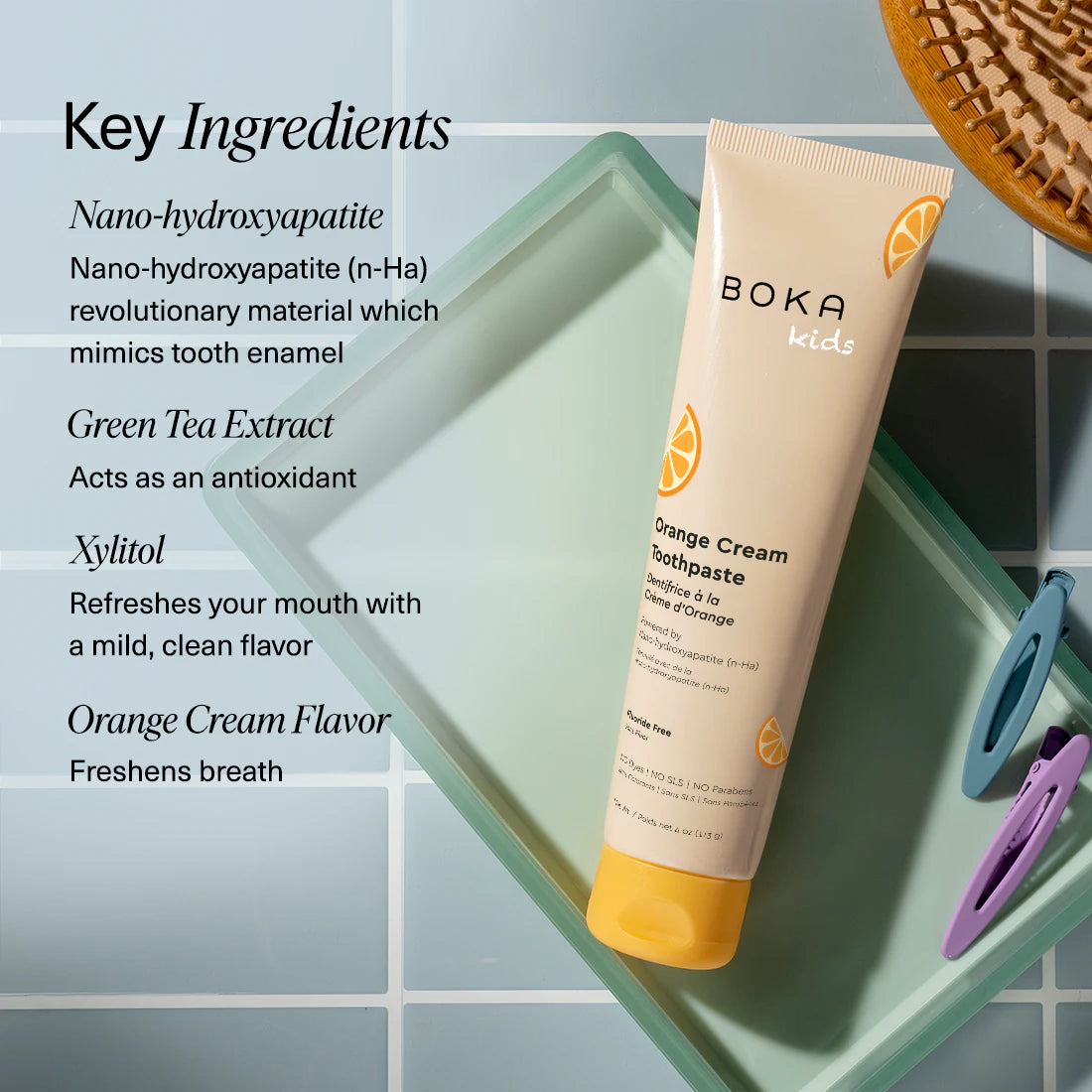 Boka Orange Cream toothpaste tube and toothbrush on a textured towel with mint leaves, alongside key ingredients listed