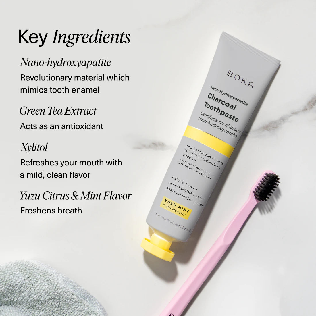 Boka Charcoal Yuzu toothpaste tube and toothbrush on a textured towel with mint leaves, alongside key ingredients listed