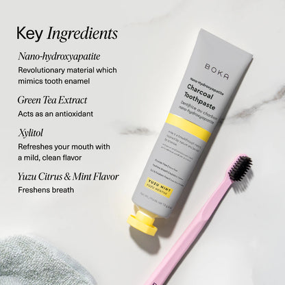 Boka Charcoal Yuzu toothpaste tube and toothbrush on a textured towel with mint leaves, alongside key ingredients listed