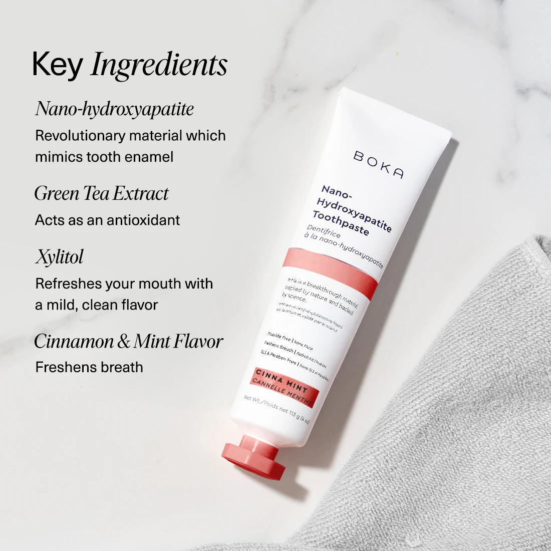 Boka Cinna Mint toothpaste tube and toothbrush on a textured towel with mint leaves, alongside key ingredients listed