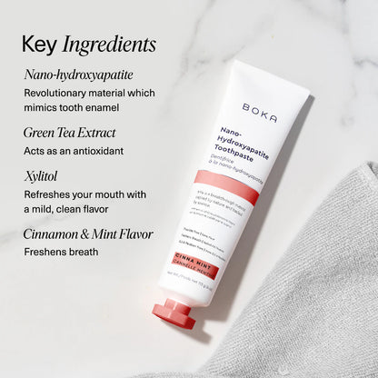 Boka Cinna Mint toothpaste tube and toothbrush on a textured towel with mint leaves, alongside key ingredients listed
