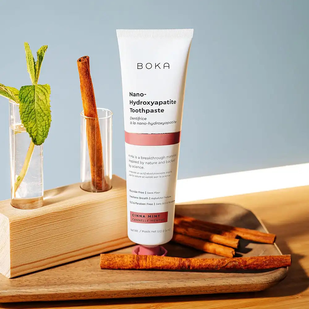 Boka Nano-Hydroxyapatite Toothpaste tube on a wooden tray with cinnamon sticks and mint leaves.