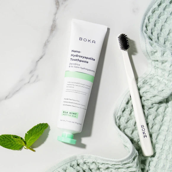 Boka toothpaste tube and toothbrush on a marble surface with mint leaves.