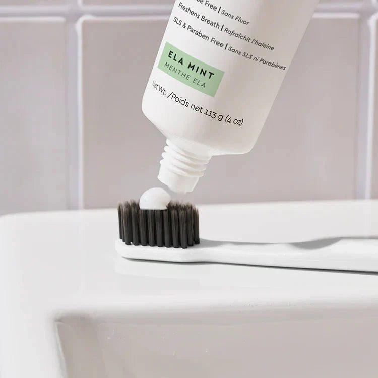 Tube of Ela Mint toothpaste being squeezed onto a toothbrush with a neutral background